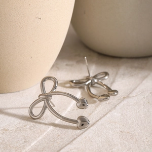 Macro shot of silver stainless steel bow and heart earrings with metallic finish