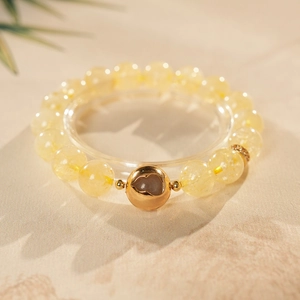 Macro detail of yellow citrine beaded bracelet with a gold metal gourd charm on a pedestal