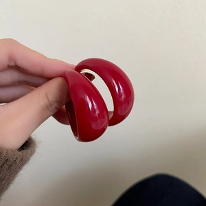 Minimalist red C-shaped hoop earrings with a glossy finish shown held in hand