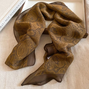 Detail view of brown paisley silk scarf necklace with translucent texture on wooden tray
