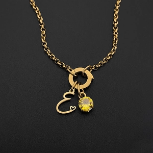 Close-up van titanium stalen ketting met gouden letter E hanger en gele edelsteen