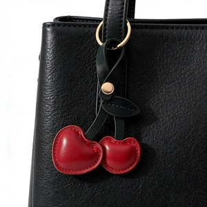 Faux leather cherry keychain pendant in red and green on a black leather handbag