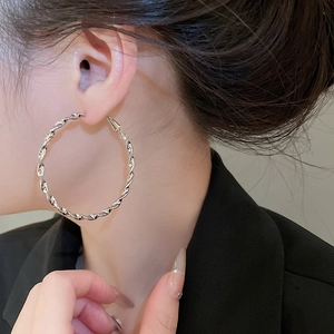 Close-up of model wearing large silver-tone twisted geometric hoop earrings with polished finish