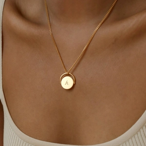 Detail of a rotating oval gold pendant featuring the letter A on a cuban chain necklace
