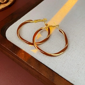 Macro shot of twisted gold-plated hoop earrings with dark brown enamel on fabric