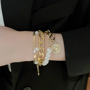 Close-up of gold OT buckle chain and pearl bracelet set layered on a wrist