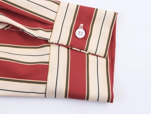 Détail du poignet d'une chemise à rayures verticales rouges avec un bouton blanc