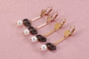 Macro detail of long pearl drop earrings with black infinity charm in rose gold finish