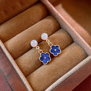 Detailed macro of gold flower earrings with blue petals and pearl on brown velvet