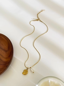 Detail of gold rose embossed pendant and white pearl on a stainless steel chain