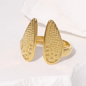 Macro detail of golden open ring featuring textured scale-like leaf charms on white stone