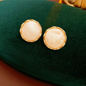 Detail of round cream marble resin earrings with gold pleated textured frames on velvet