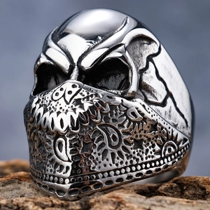 Polished silver skull ring with ornate mask relief on natural wood background