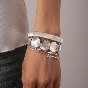 Detail of silver layered metal bracelets set including textured mesh and hammered bangles