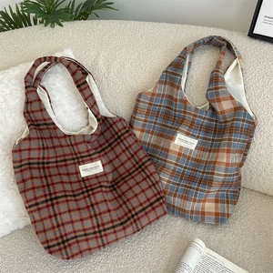 Detail of plaid canvas tote bags in red-brown and blue-grey with stitched brand labels