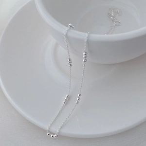 Detailed view of S925 sterling silver beaded necklace draped on white ceramic cup