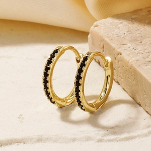 Elegant gold hoop earrings with black zircon stones on a beige stone and silk background