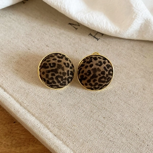 Detail of round leopard print stud earrings with elegant gold trim on linen fabric