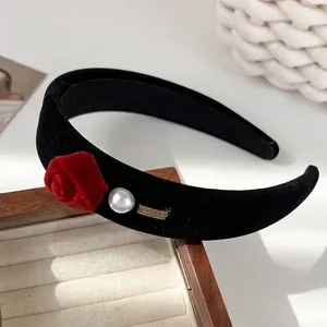 Detail of black velvet headband featuring a red rose, white pearl and golden metal tag