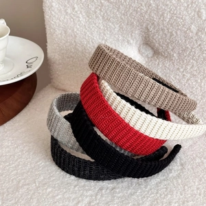Five knit headbands in neutral colors and red displayed on a cozy plush chair