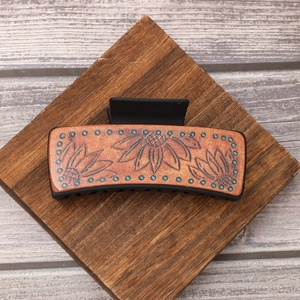Western style leather hair claw clip with sunflower pattern on a vintage wooden block