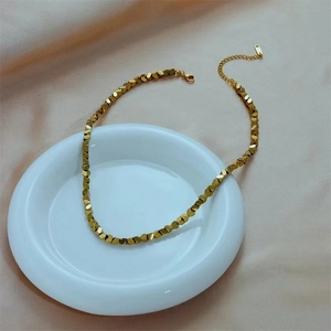 Minimalist gold faceted beaded necklace displayed on a white ceramic plate with silk fabric