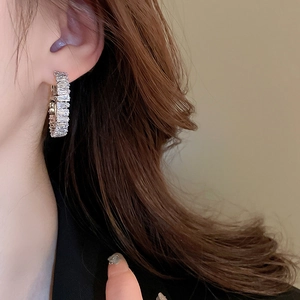 Close-up of luxury hoop earrings with rectangle-cut zircon stones worn by a model