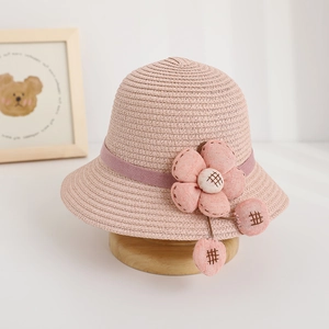 Detailed view of pink woven straw sun hat featuring a large fabric flower and small pom-poms