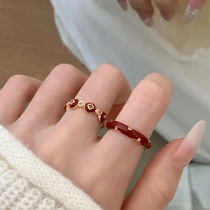 Detail view of red enamel rings with gold clover pattern on white knit background