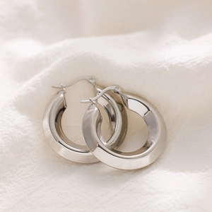 Close-up of polished silver chunky hoop earrings on a white soft textured fabric