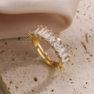Close-up of adjustable gold ring with white baguette zircon on beige stone surface