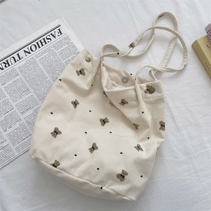 Close-up of corduroy tote bag with bear print and button closure on white linen