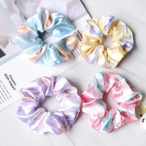 Set of four satin tie-dye hair scrunchies in vibrant pastel colors on marble surface