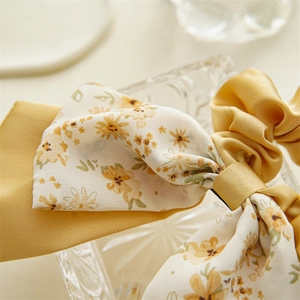 Detail of floral chiffon and yellow satin fabric texture on a double-layered bow hair tie