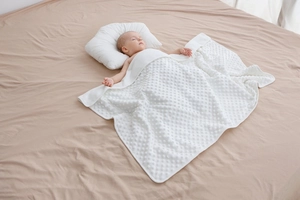 Dettaglio coperta neonato a bolle bianca e cuscino a nuvola su letto beige