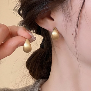 Close-up of matte gold teardrop stud earrings worn by a model for a minimal look