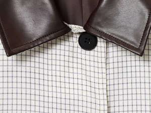 Détail du col en cuir marron foncé et texture à carreaux avec un bouton noir