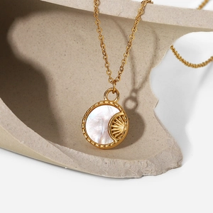 Detail of a gold plated round necklace with white mother of pearl moon pendant on stone