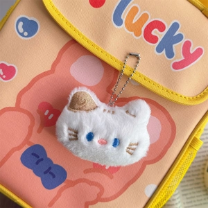 Close-up of white plush cat head charm with blue eyes on a canvas lucky bag