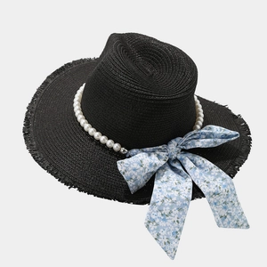 Close-up of black raffia sun hat featuring pearl chain and large blue floral bow detail