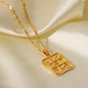 Detail of gold rectangular pendant with mesh texture and inlaid crystals on silk