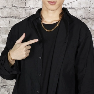Golden Cuban link necklace and bracelet set for men worn on a black shirt with brick backdrop