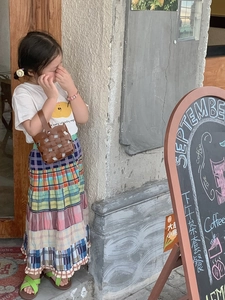 Detail of child wearing a brown woven bucket bag with a patchwork tiered maxi skirt