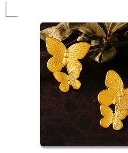 Detailed close-up of golden butterfly titanium steel earrings on a vintage leather backdrop