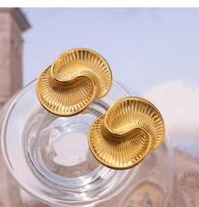 Macro detail of golden teardrop earrings with spiral texture and radiant sunburst engraving
