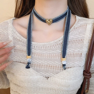 Close-up of denim choker with gold heart pendant and hanging decorative beads