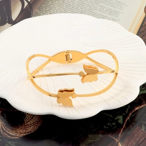 Detailed macro view of gold butterfly stainless steel bangle on a decorative shell plate