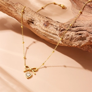 Collier élégant doré avec pendentif cœur noeud et cristaux sur support en bois naturel