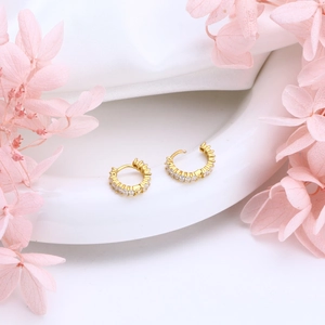 Detail of gold hoop earrings with square-cut zircons on an elegant pink floral display