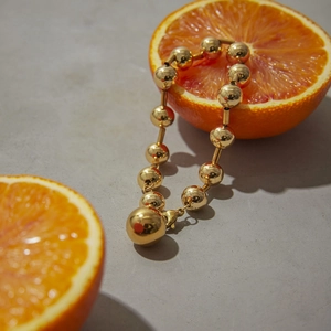 Gros plan d'un bracelet à billes dorées polies drapé sur une orange fraîche coupée